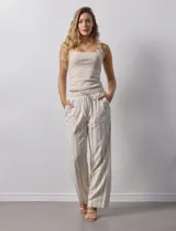 Pantalón de lino a rayas verticales color beige y blanco, con pretina ancha elastizada, lazo de ajuste y bolsillos inclinados.