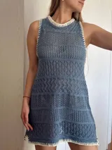 Vestido corto tejido con hilo de algodón color beige, con cuello redondo y sin mangas. Presenta un diseño calado con franjas horizontales y silueta recta.