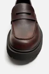 Mocasín de cuero color marrón oscuro, con antifaz y suela track de goma negra.