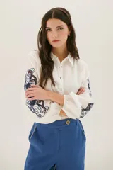 Camisa blanca de manga larga con bordados florales marrones en las mangas.