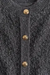 Cárdigan gris oscuro de tejido de punto con textura, cuello redondo, cierre frontal con botones dorados y terminaciones acanaladas en cuello, puños y bajo.
