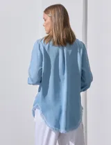 Camisa de jean celeste con flecos en el ruedo, de mangas largas y corte recto.