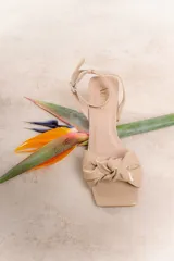 Sandalia negra de charol con taco cuadrado, tira fina al tobillo con hebilla y moño trenzado en el empeine.