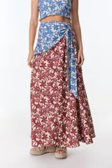 Falda larga con estampado floral en tonos rojo y beige, con detalle de tela azul estampada anudada en la cintura.