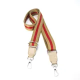 Correa de tela color beige con dos franjas rojas, con herrajes plateados y detalles en cuero sintético color beige.