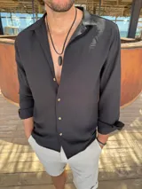 Camisa negra de fibrana, de corte clásico, con cuello camisero, manga larga con puños abotonados y cierre frontal con botones.