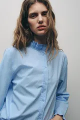 Camisa blanca de algodón con cuello con volantes y mangas largas con puños fruncidos.
