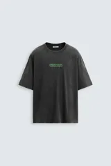 Camiseta negra con efecto lavado, corte relaxed fit, cuello redondo y manga corta. Estampado frontal y trasero con textos en verde.