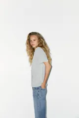 Camiseta gris de algodón con cuello redondo y manga corta. Tiene apliques de strass plateado en el frente.
