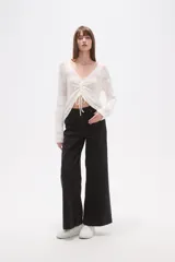 Sweater de poliéster color beige, con cuello en V, manga larga y frunces ajustables en el frente. Presenta un diseño de tejido calado.