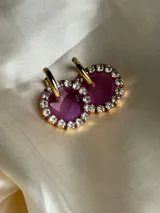 Par de aros colgantes con dije circular de resina con glitter multicolor y borde de strass. El arito es de acero quirúrgico dorado.