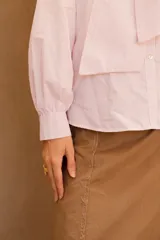 Camisa de algodón a rayas verticales rosas y blancas, con cuello alto y lazo grande en el cuello.