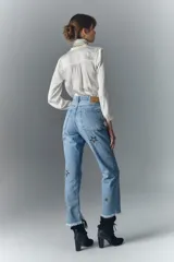 Pantalón de jean de tiro alto, denim azul rígido con lavado localizado y apliques de brillos. Pierna recta y ruedo desflecado.