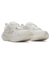 Zapatillas deportivas Under Armour modelo Assert 11 para mujer, color blanco hueso, con logo UA en el lateral. Presentan una suela gruesa con tecnología Charged+® y una combinación de malla transpirable y revestimientos de cuero sintético.