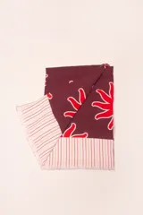 Pareo rectangular de viscosa con estampado de flores rojas sobre fondo borgoña y borde inferior con rayas verticales rojas, amarillas y blancas.