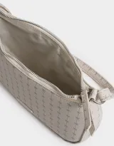 Bandolera tipo baguette color crema con estampado de moños en gris. Tiene asa corta para llevar al hombro, cierre superior y tag metálico con logo.