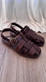 Sandalias de cuero color marrón con tiras entrecruzadas y hebilla metálica.