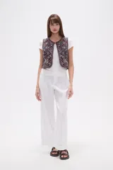 Chaleco sin mangas, sin abroches, con escote redondo. Confeccionado en tejido oscuro con bordados geométricos y florales en tonos rojos, blancos, azules y mostaza, con apliques de cuentas.