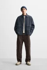 Camisa de hombre a cuadros azules y negros, de corte cuadrado, con cuello solapa, manga larga con puños abotonados, cierre frontal con botones y bolsillos de parche con solapa en el pecho.