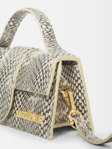 Bolso pequeño estructurado con estampado de piel de serpiente en tonos blanco y negro, con asa superior acolchada y correa larga extraíble. Cierre magnético con solapa, bolsillo trasero y herrajes dorados.