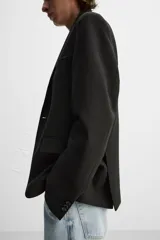 Blazer negro de corte regular fit, confeccionado en tejido con viscosa. Presenta cuello con solapas de muesca, manga larga con puños abotonados, bolsillo de vivo en el pecho, bolsillos de solapa en la cadera, bolsillo interior, aberturas en la espalda y cierre frontal con dos botones.