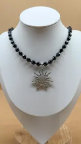 Collar corto de cuentas facetadas negras con dije de sol plateado con circonitas.