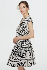 Vestido corto sin mangas de algodón color crudo con estampado de flores, hojas y lunares en negro. Tiene escote cruzado en V, cintura elastizada y falda con vuelo.
