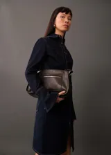 Bolso bandolera de cuero color marrón oscuro, con correa ajustable y cierre superior con cremallera.