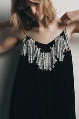 Vestido midi negro de tejido plisado, con escote pico, tirantes finos ajustables y aplicación de encaje y bordados florales combinados a contraste.