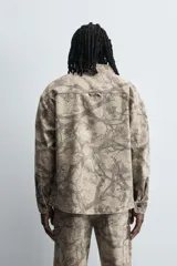 Sobrecamisa color beige con estampado abstracto en tonos grises, de corte relaxed fit, cuello solapa, manga larga con puños abotonados, bolsillos de plastrón en el pecho, efecto lavado y cierre frontal con botones.