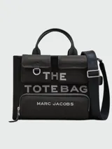 Bolso tote mediano de lona color beige con detalles en negro. Tiene doble asa de mano de cuero y correa bandolera ajustable y extraíble. Cuenta con dos bolsillos frontales con solapa y un bolsillo frontal con cierre. Estampado frontal con la leyenda "THE TOTE BAG" y el logo "MARC JACOBS".