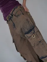 Pantalón cargo de jean color marrón con efecto desgastado, múltiples bolsillos funcionales y detalles metálicos en bronce.