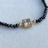 Pulsera elástica con cuentas de piedra natural espinela negra, cuentas alternadas goldfilled y dije cuadrado con cristal y acero.