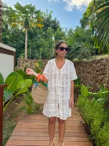 Vestido playero blanco de tejido calado tipo encaje de algodón, corte recto y suelto, con mangas cortas, escote en V y botonadura frontal.