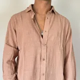 Camisa de lino color beige, de corte oversize, con cuello clásico y mangas largas con puños abotonados.
