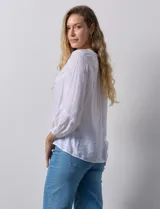 Blusa blanca de gasa bambula con cuello a la base y apertura central con botones. Apliques de crochet en la parte delantera y en las mangas ¾ con terminación fruncida.