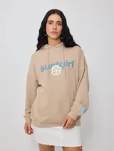 Canguro beige con capucha, estampado frontal con el texto "Australian Surfgirl Rusty" y un hibisco blanco.