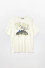 Remera unisex de algodón lavado color beige claro, con cuello redondo y manga corta. Presenta un estampado frontal con texto en dorado que dice "ENFOQUE" y "MOVIMIENTO", y una figura humana en tonos grises y un círculo azul.