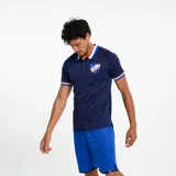 Polo deportivo azul marino con cuello tipo camisa y tres botones. Los bordes de las mangas y el cuello tienen detalles de rayas blancas y rojas. Lleva el escudo del Club Nacional de Football bordado en el pecho.