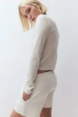 Saco color blanco hueso de punto pointelle suave, entallado, con cuello redondo y abotonadura frontal.