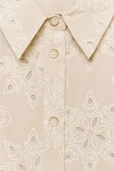 Vestido corto color beige con bordados florales perforados, cuello solapa, sin mangas, cinturón de tela con hebilla redonda y cierre frontal con botones.