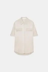 Camisa color beige de cuello solapa y manga corta. Tiene dos bolsillos delanteros con solapa y cierre frontal con botones.