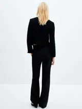 Chaqueta negra de tweed con cuello redondo, cierre frontal con botones dorados, bolsillos de parche y flecos en el ruedo.