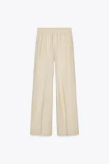 Pantalón color beige de lino, de tiro alto con cintura elástica, bolsillos laterales ocultos en costura y pernera ancha.