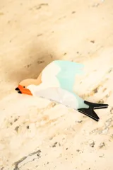 Broche con forma de colibrí con cuerpo blanco, cabeza naranja, pico negro, ala celeste y cola negra.