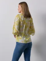 Blusa de gasa verde con estampado de flores blancas y celestes. Tiene cuello a la base con escote en V y mangas 3/4 fruncidas.