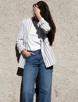 Blazer blanco con rayas verticales negras, cuello con solapa, bolsillos simulados y mangas 3/4 fruncidas. Forro interno blanco, marca Dictionary.