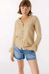 Blusa blanca de lino con botones de nácar, volados en el escote y mangas largas con puños acampanados. Corte recto y holgado.