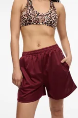 Short deportivo color bordó de tela satinada con cintura elastizada, bolsillos laterales y franja lateral blanca.