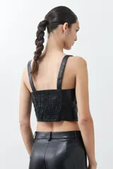 Top negro de eco cuero con corte crop, breteles finos y detalle de tul en el escote.
